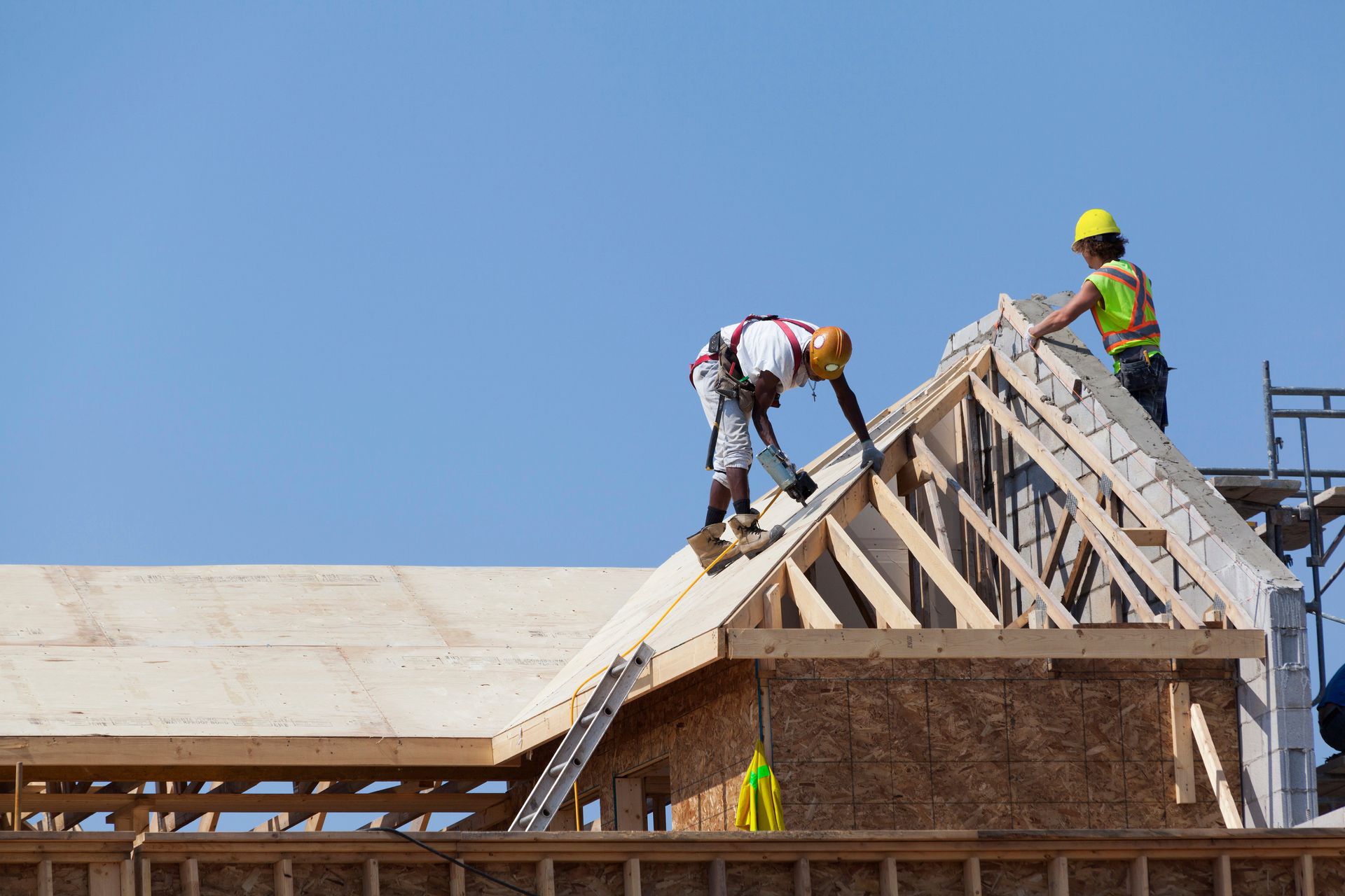Construction workers on a roof framing a house under a clear blue sky