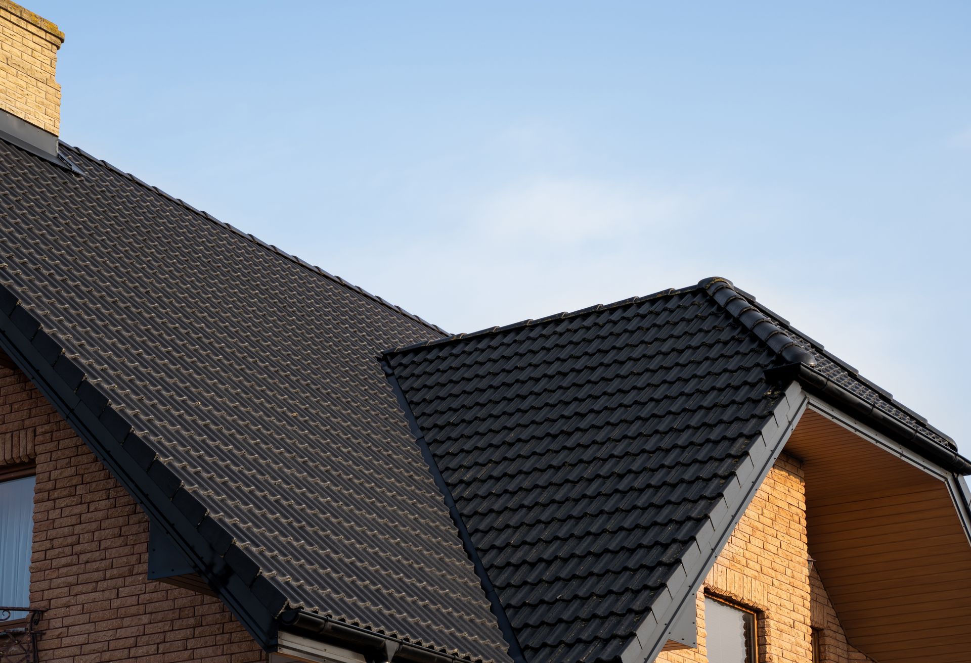 Roof of a brick house with dark gray tiled sections against a blue sky Roof of a brick house with dark gray tiled sections against a blue sky