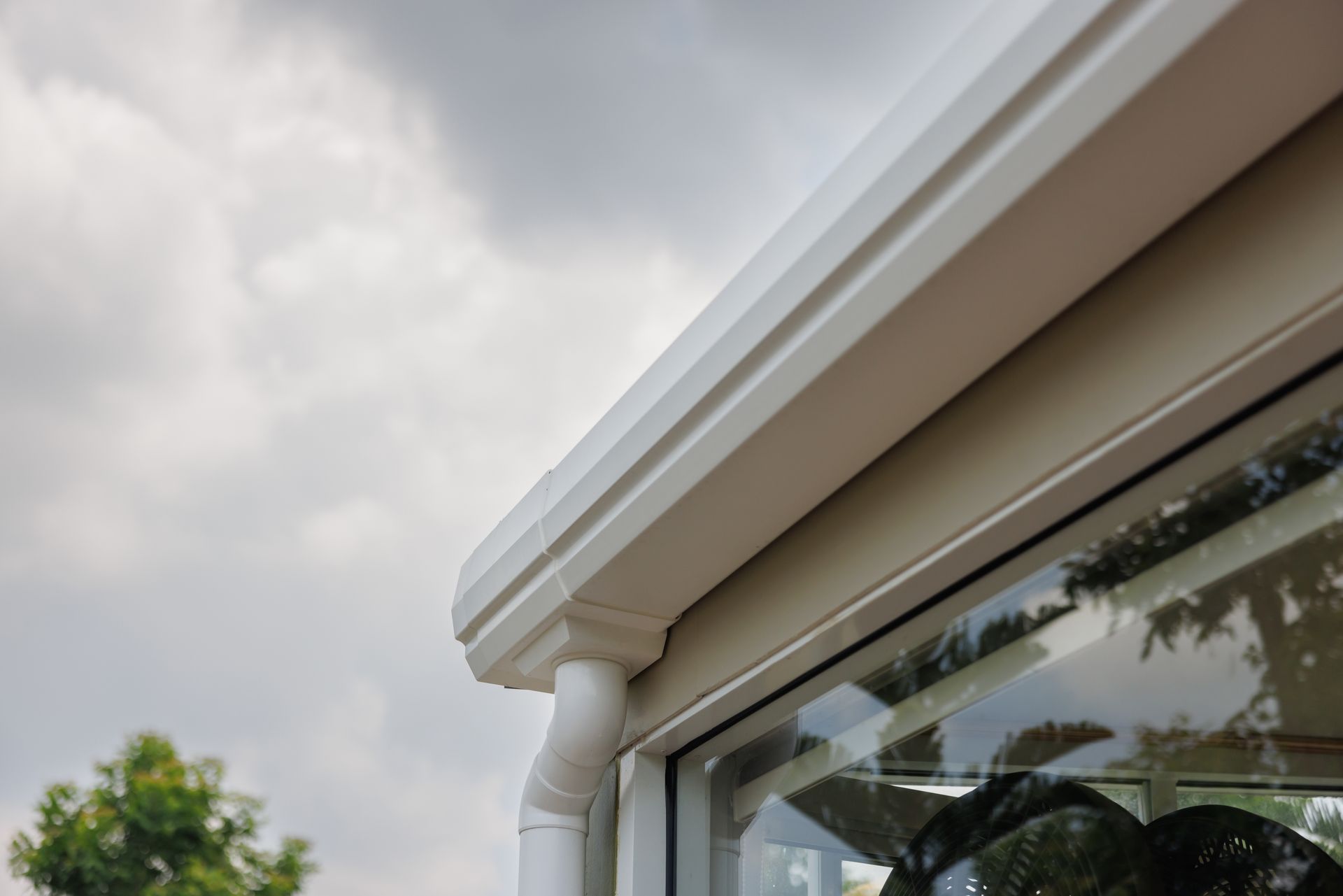 Close-up of a white house gutter and roof edge against a cloudy sky