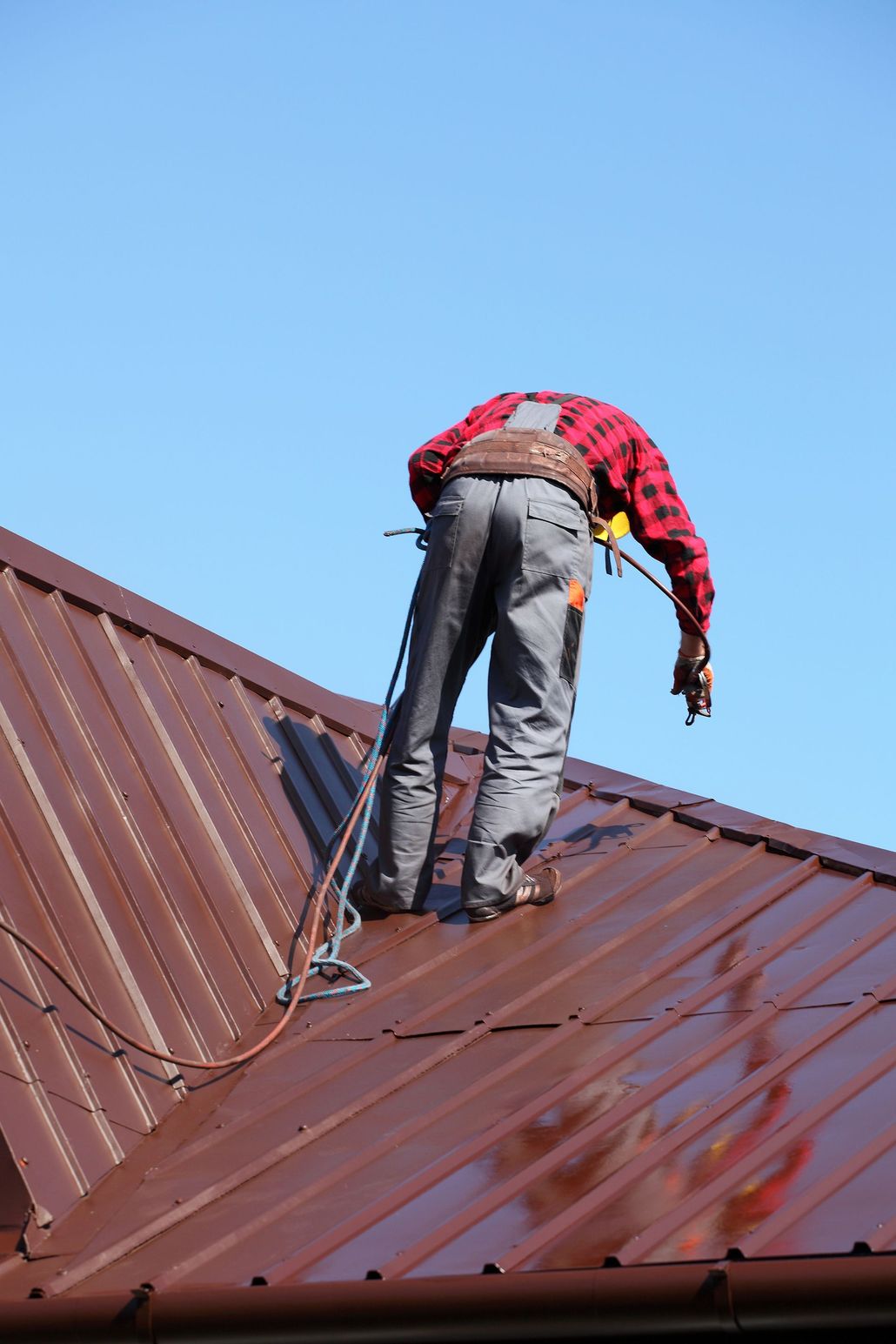 Worker on a metal roof inspecting or repairing it under a clear blue sky Worker on a metal roof inspecting or repairing it under a clear blue sky