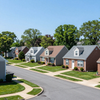 Quiet suburban street with neat single-family houses, green lawns, and a clear blue sky