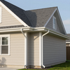 Beige house exterior with gray shingled roof and white trim, showing side walls and windows.