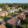 Aerial view of a quiet suburban neighborhood with brick houses, tree-lined streets, and rooftops in warm sunlight.