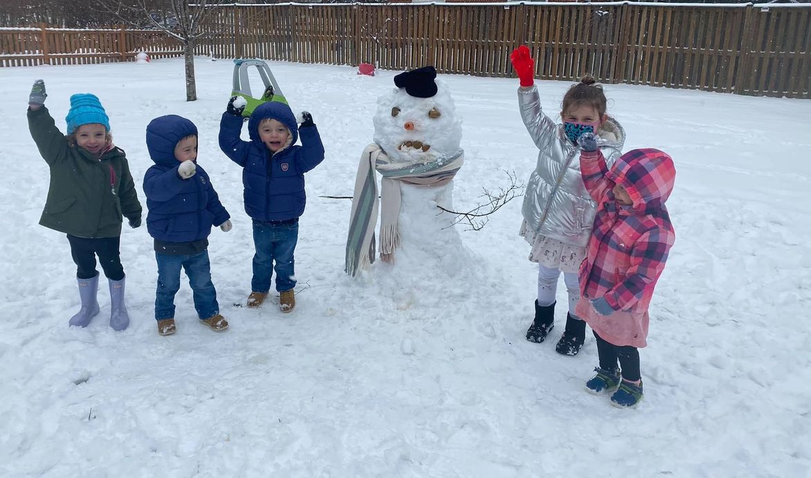 Children playing in the snow beside a snowman, waving colorful mittens in a snowy park