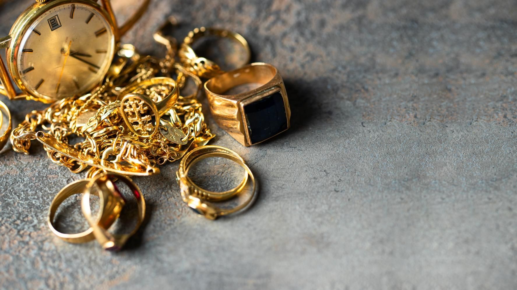 A pile of gold jewelry including a watch and rings on a table.