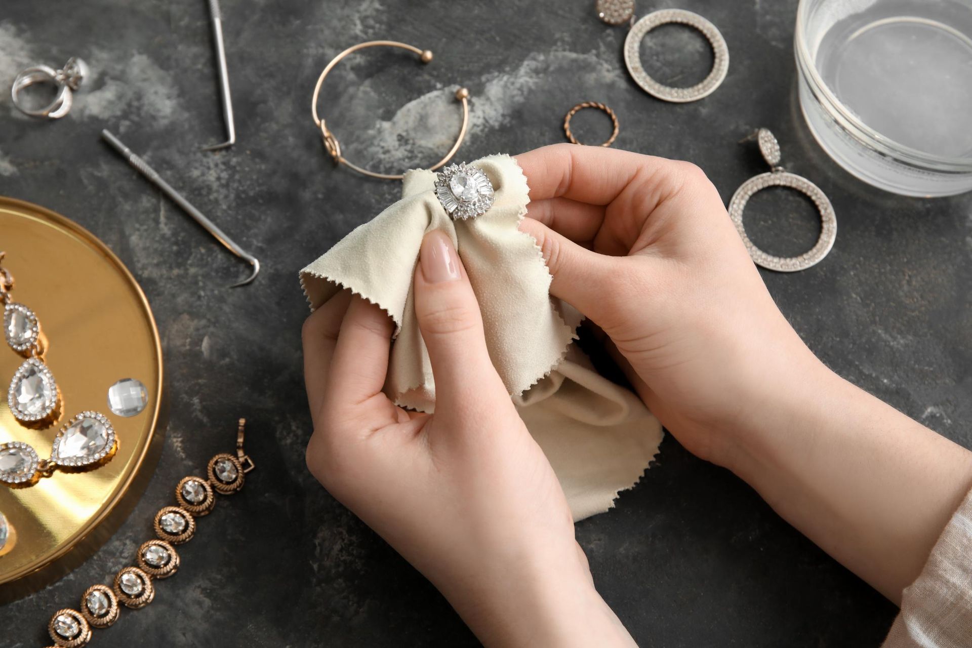 A woman is cleaning jewelry with a cloth on a table.