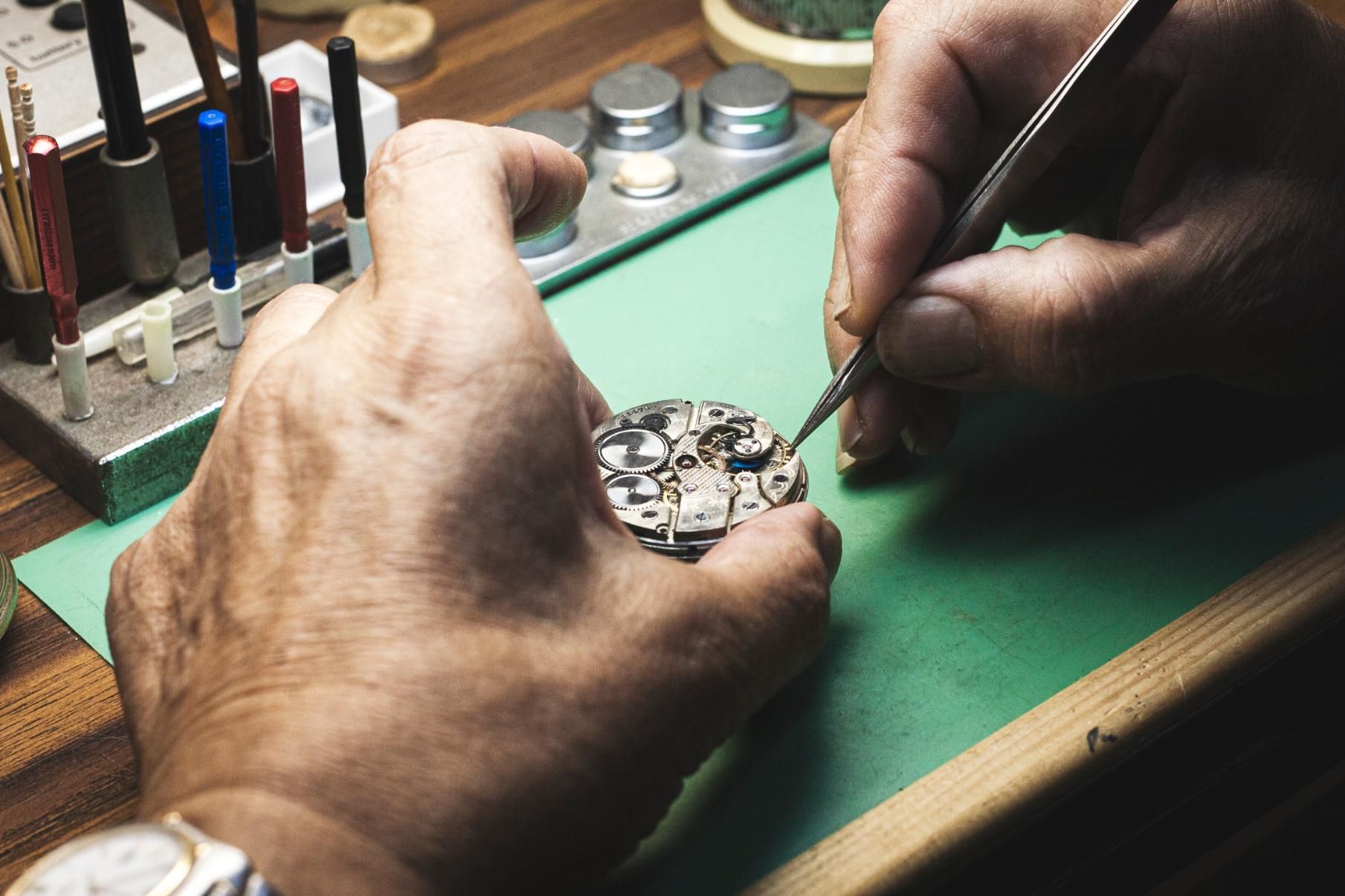 A man is working on a watch on a green table.