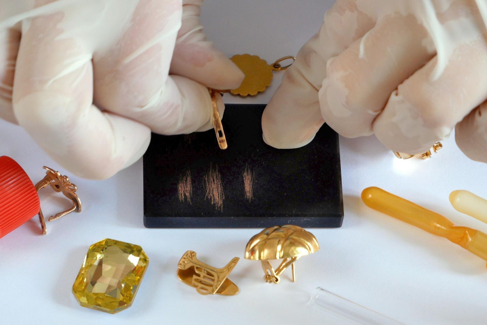 A person wearing gloves is holding a piece of gold jewelry.