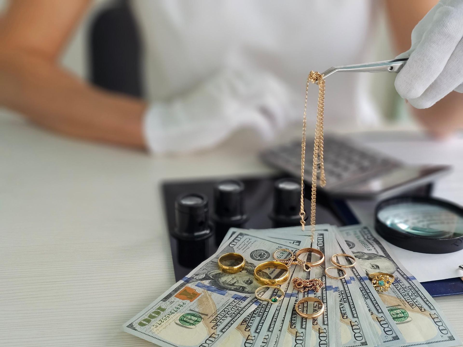 A woman is holding a pair of tweezers over a pile of money and jewelry.