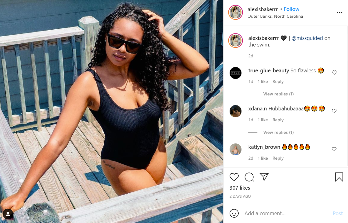 A person in a black one-piece swimsuit poses on a wooden staircase outdoors on a sunny day.