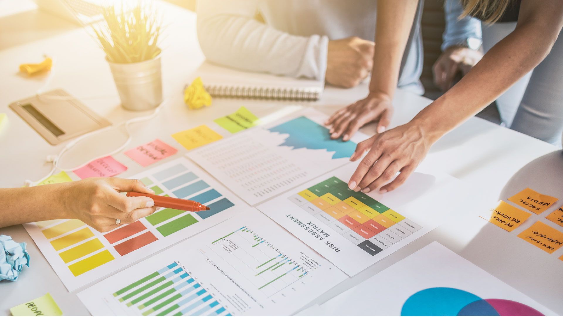 Hands reviewing colorful charts and graphs spread across a bright office desk