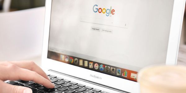 A person typing on a laptop with the Google search homepage displayed on the screen.