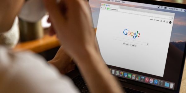 A person sitting at a laptop with the Google homepage open on the screen.