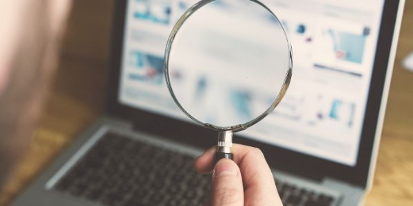 A hand holds a magnifying glass over a laptop screen, focusing on digital content.