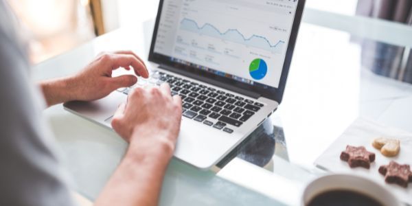 A person typing on a laptop displaying data charts, sitting at a table with coffee and cookies.