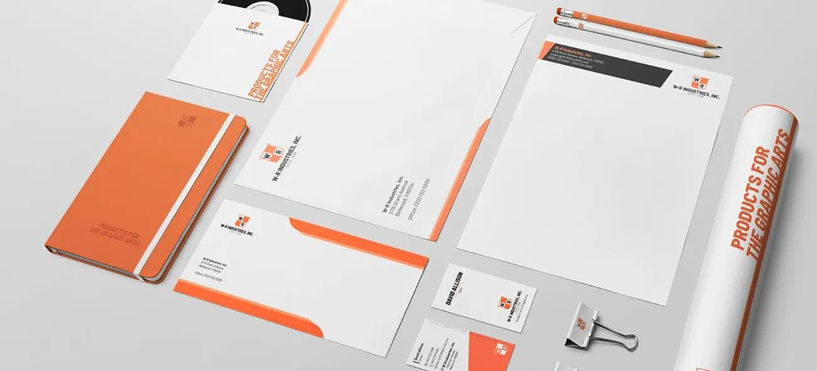 A mockup of corporate stationery and office supplies, featuring orange and white branding on paper, a notebook, and a tube.