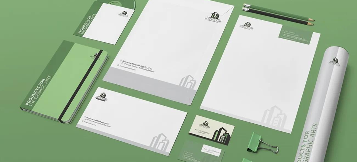 A branding mockup featuring stationery, a notebook, business cards, a pen, and a paper tube on a sage green background.