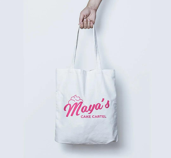 A white tote bag held by a hand, featuring a pink logo that reads 