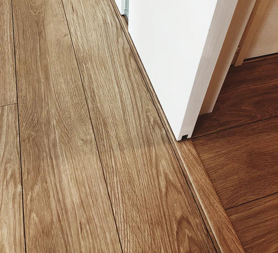 A light-colored wooden floor meeting a darker wooden floor at a white doorway threshold with a transition strip.