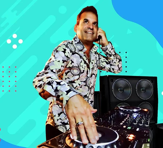 A DJ in a patterned shirt with headphones on, mixing music on a turntable in front of a speaker against a teal background.