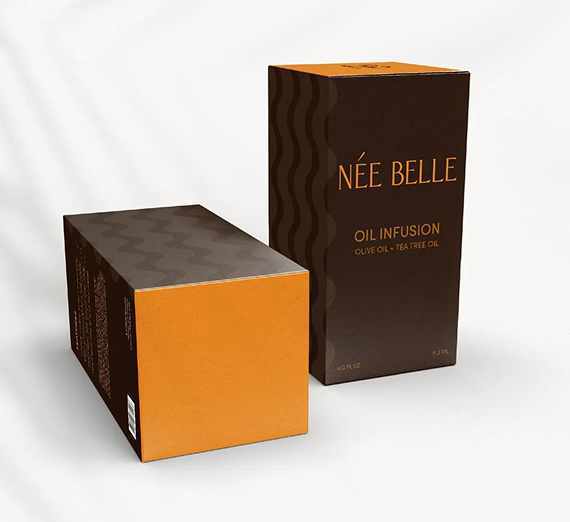 Two rectangular Née Belle oil infusion boxes, one standing upright and one lying on its side, in brown and gold tones.