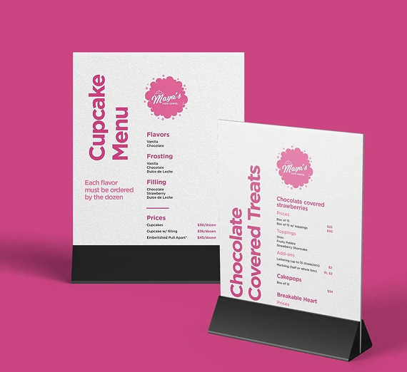 Two white menu signs for a dessert shop, labeled Cupcake Menu and Chocolate Covered Treats, on a solid pink background.