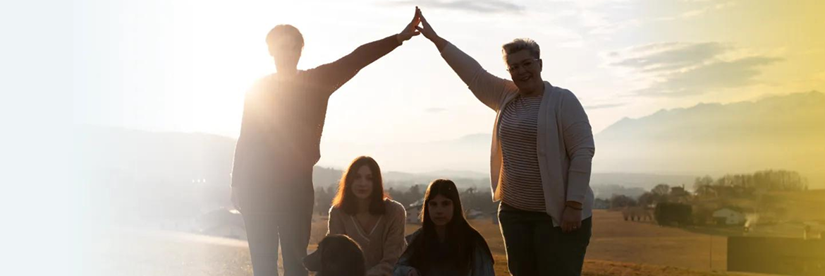 Four people stand outside at sunset, with two standing on the ends forming a roof shape with their joined hands above them.