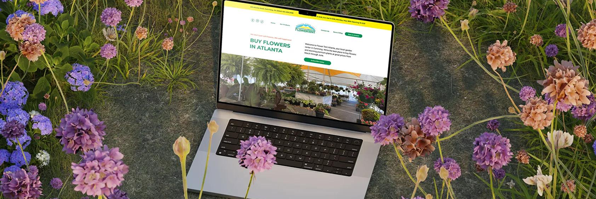 A laptop displaying a landscape website rests open in a field of purple flowers and greenery.