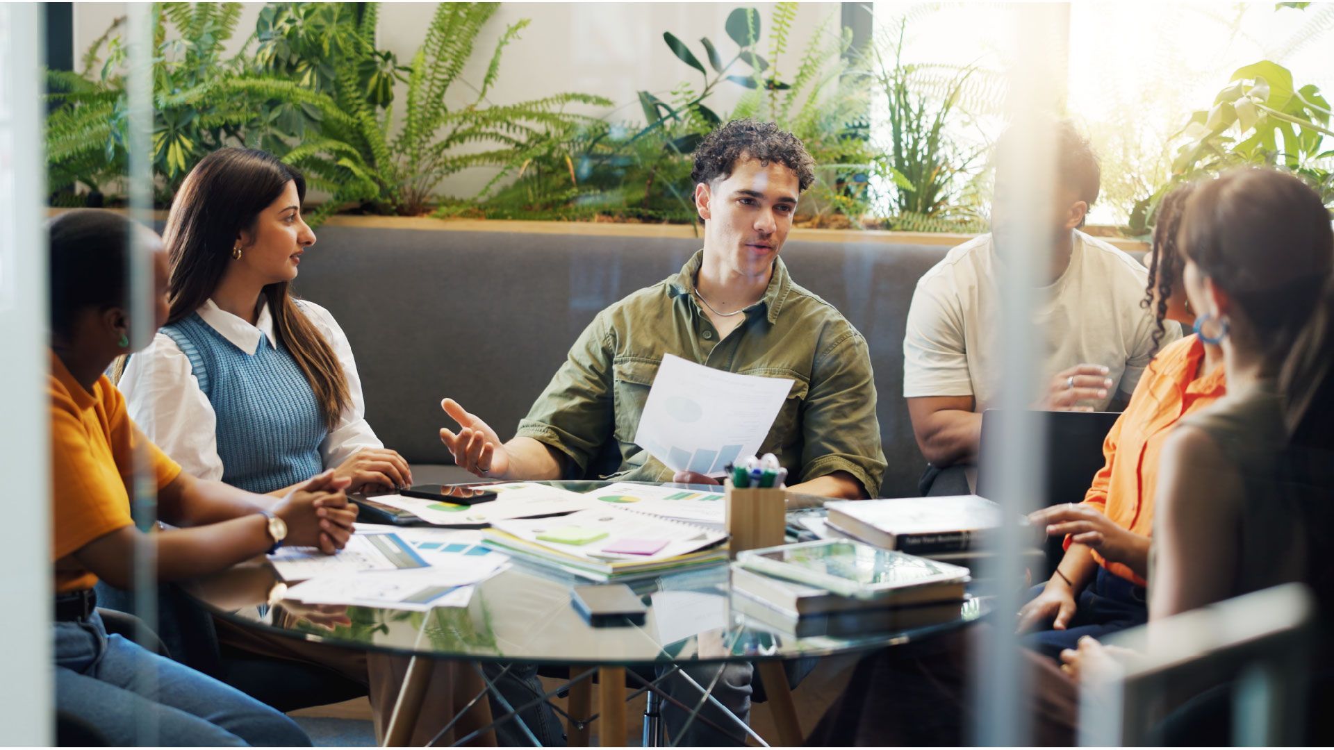 Small group meeting around a table, reviewing papers in a bright indoor lounge.