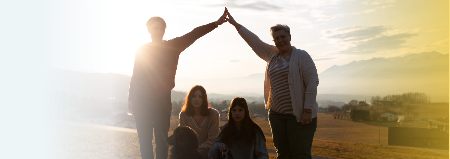 Four people stand outside at sunset, with two standing on the ends forming a roof shape with their joined hands above them.
