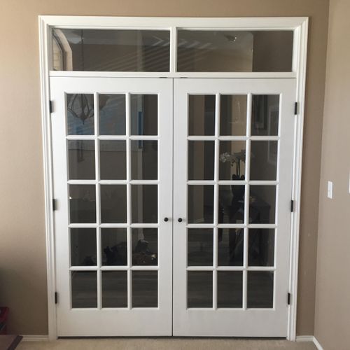 A pair of french doors in a room with a window above them.
