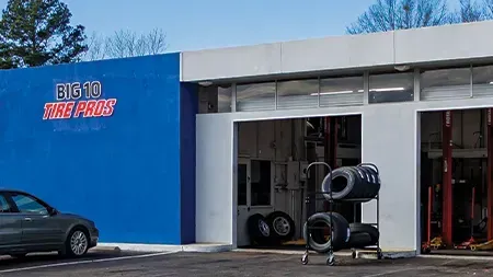 Big 10 Tire Pros shop with blue wall, gray car, tires, and open bay.