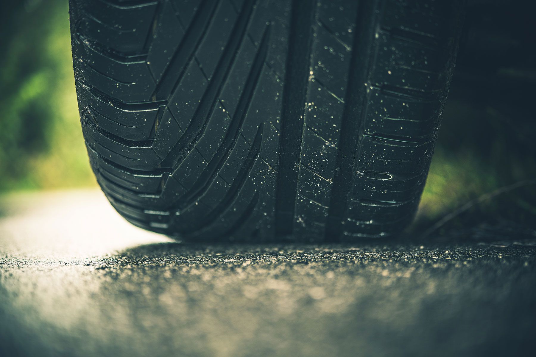 Close-up of a black tire on a wet asphalt road, highlighting the tread pattern.