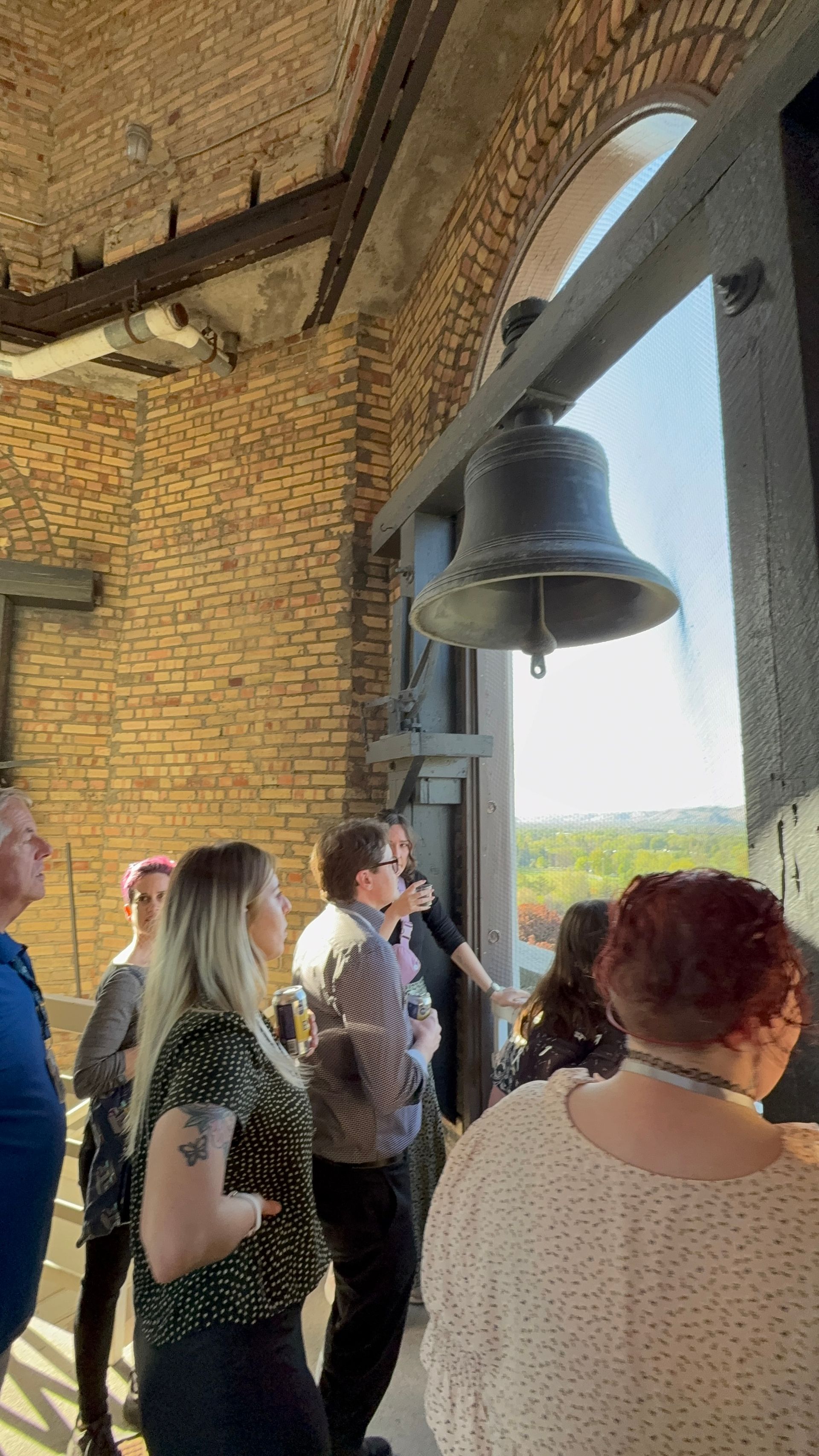 People looking up at a large bell in a brick tower window. Sunlight streams in Boise Idaho
