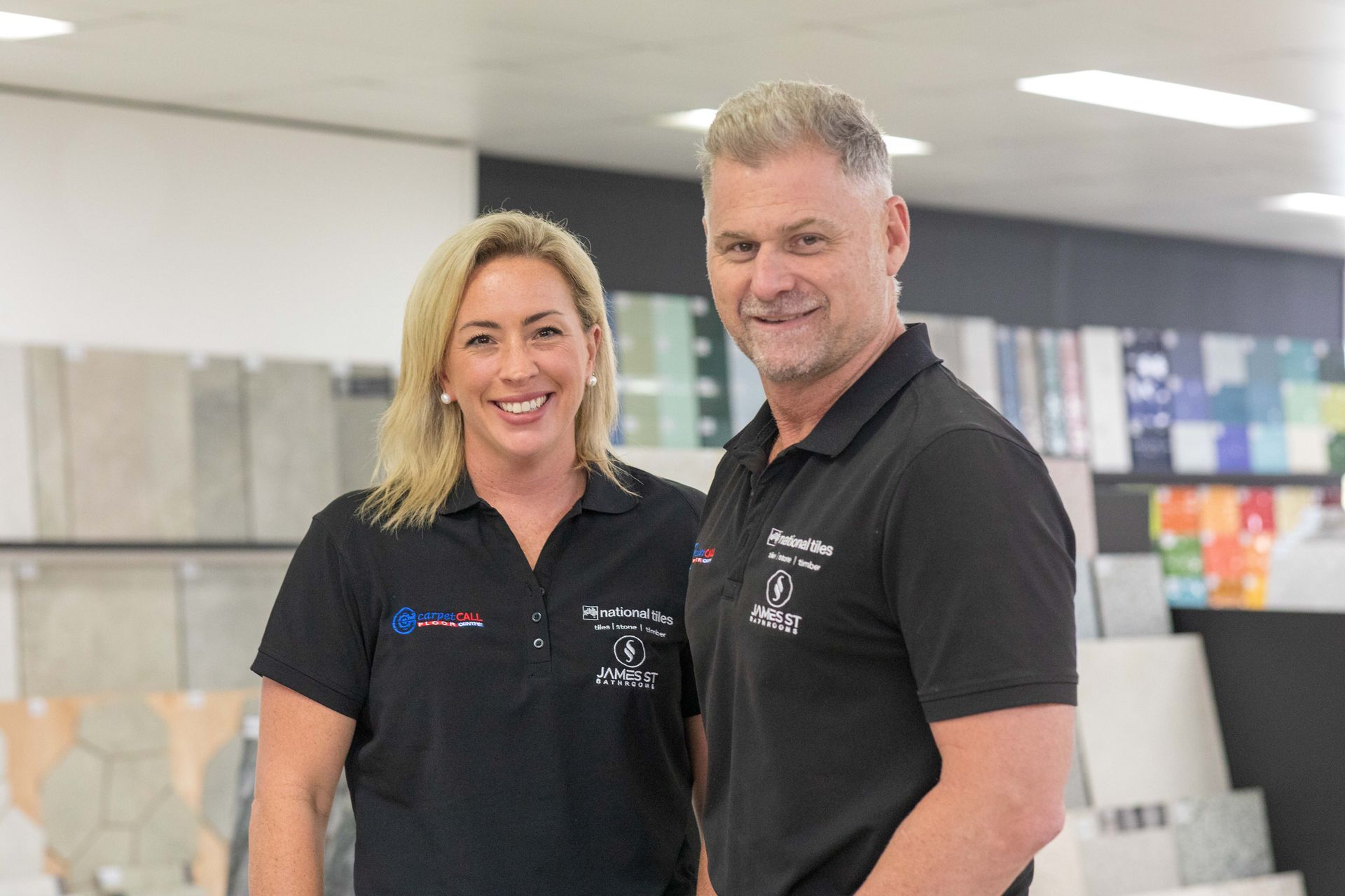 Two people smiling in a showroom, woman on the left, man on the right, both wearing black shirts.