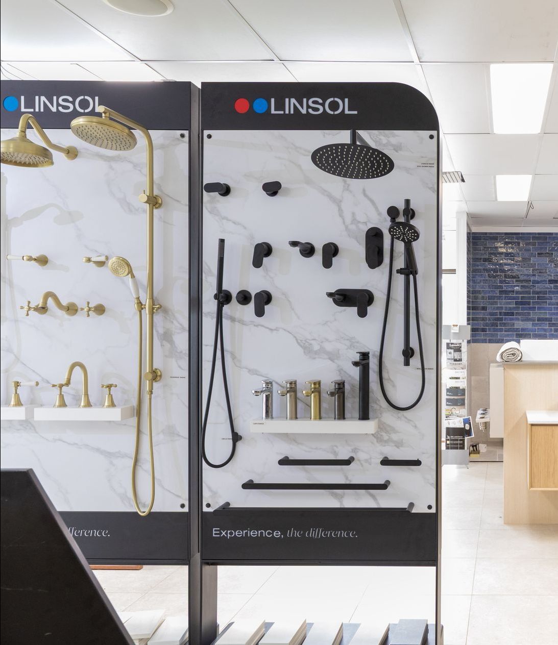 Shower fixtures display in a showroom, gold and matte black finishes against marble-look panels.