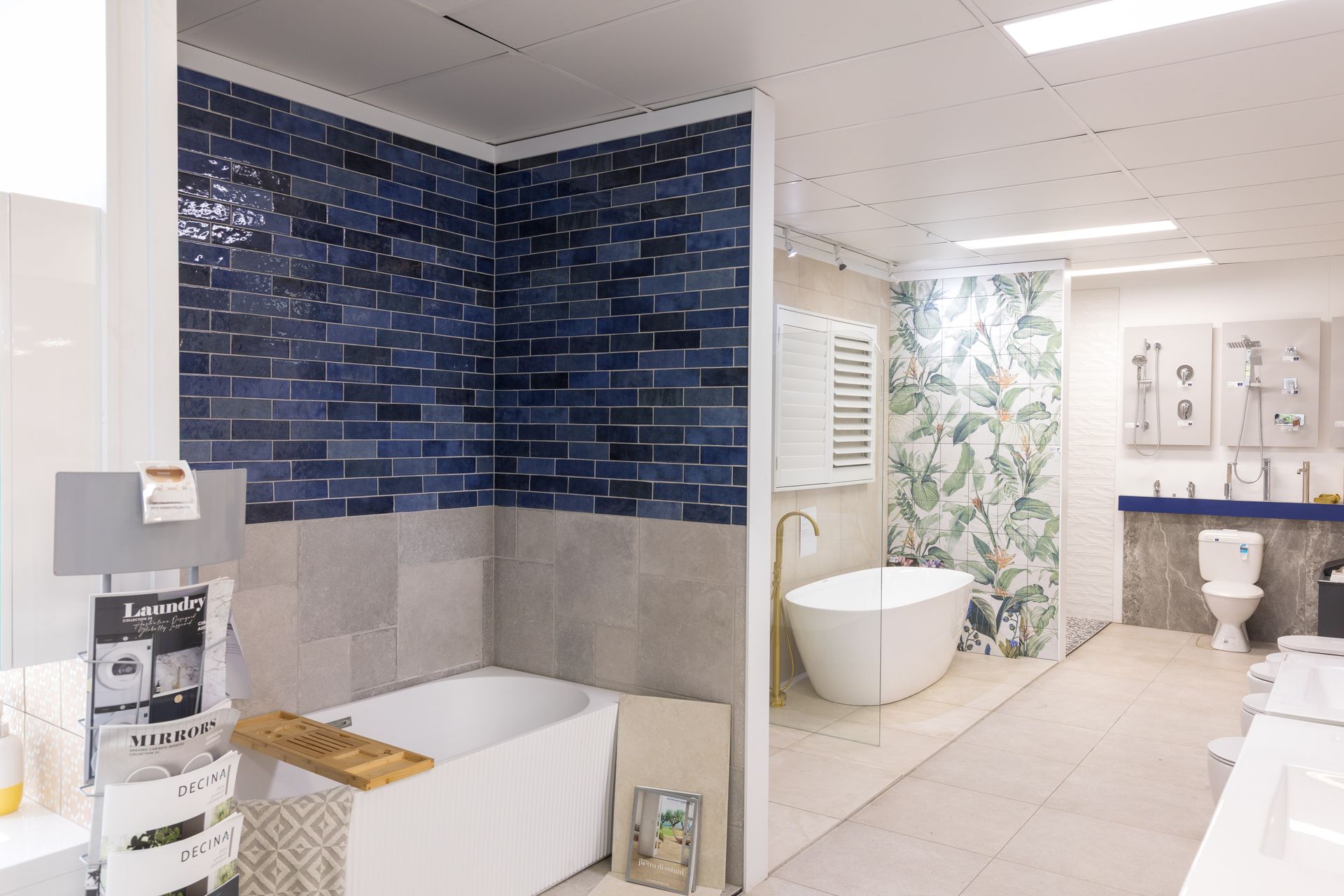 Bathroom showroom with tile and bathtub displays; blue and grey tile; white tub; bright lighting.