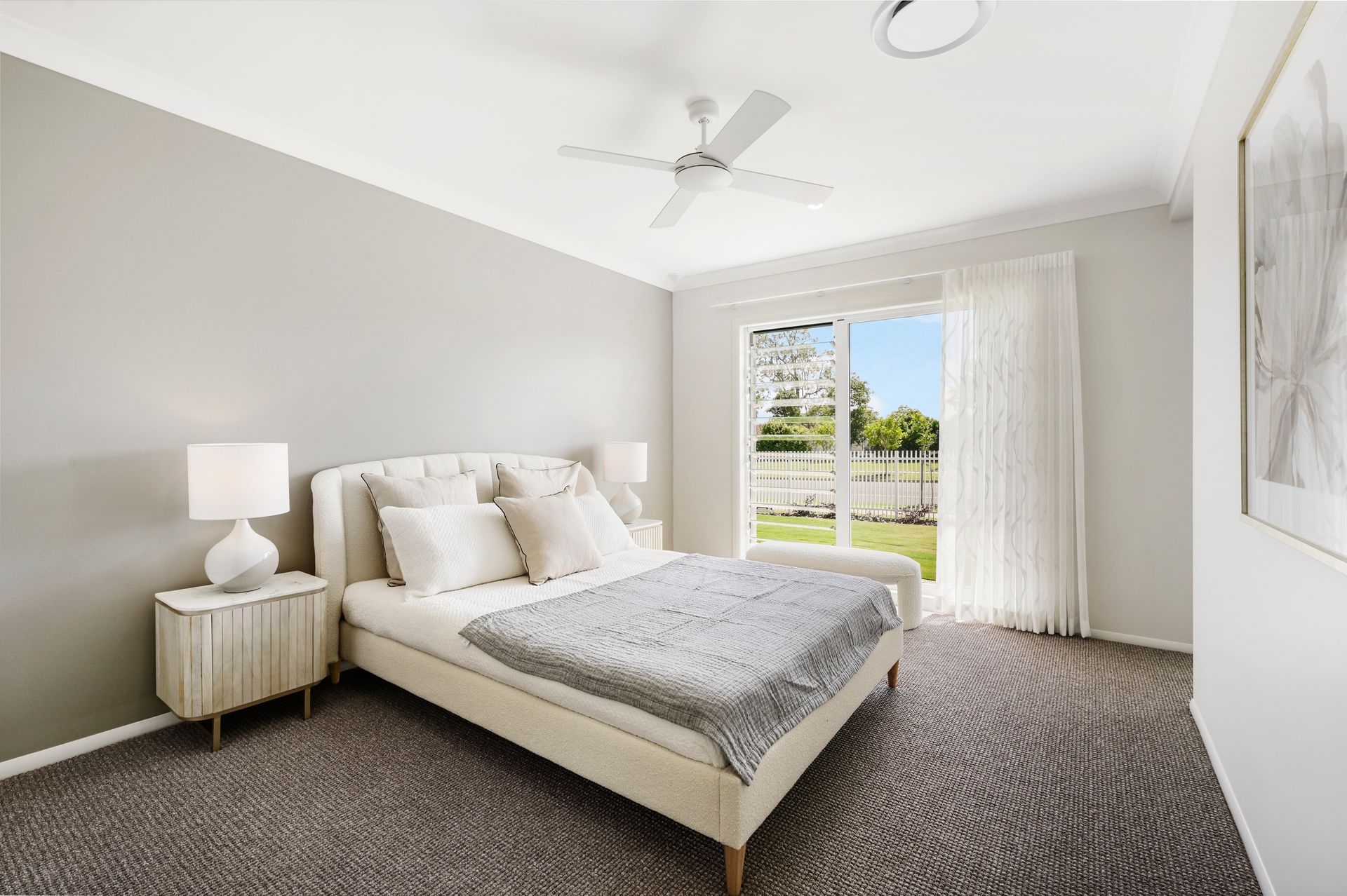 Bedroom with a bed, bedside tables, window, and a grey patterned carpet. Light grey walls and white ceiling.