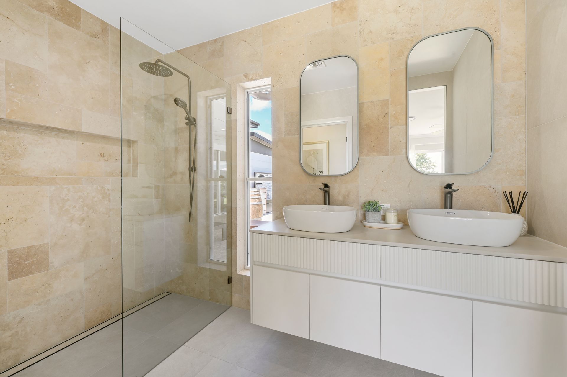 Modern bathroom with beige walls, double sinks, and a glass shower.