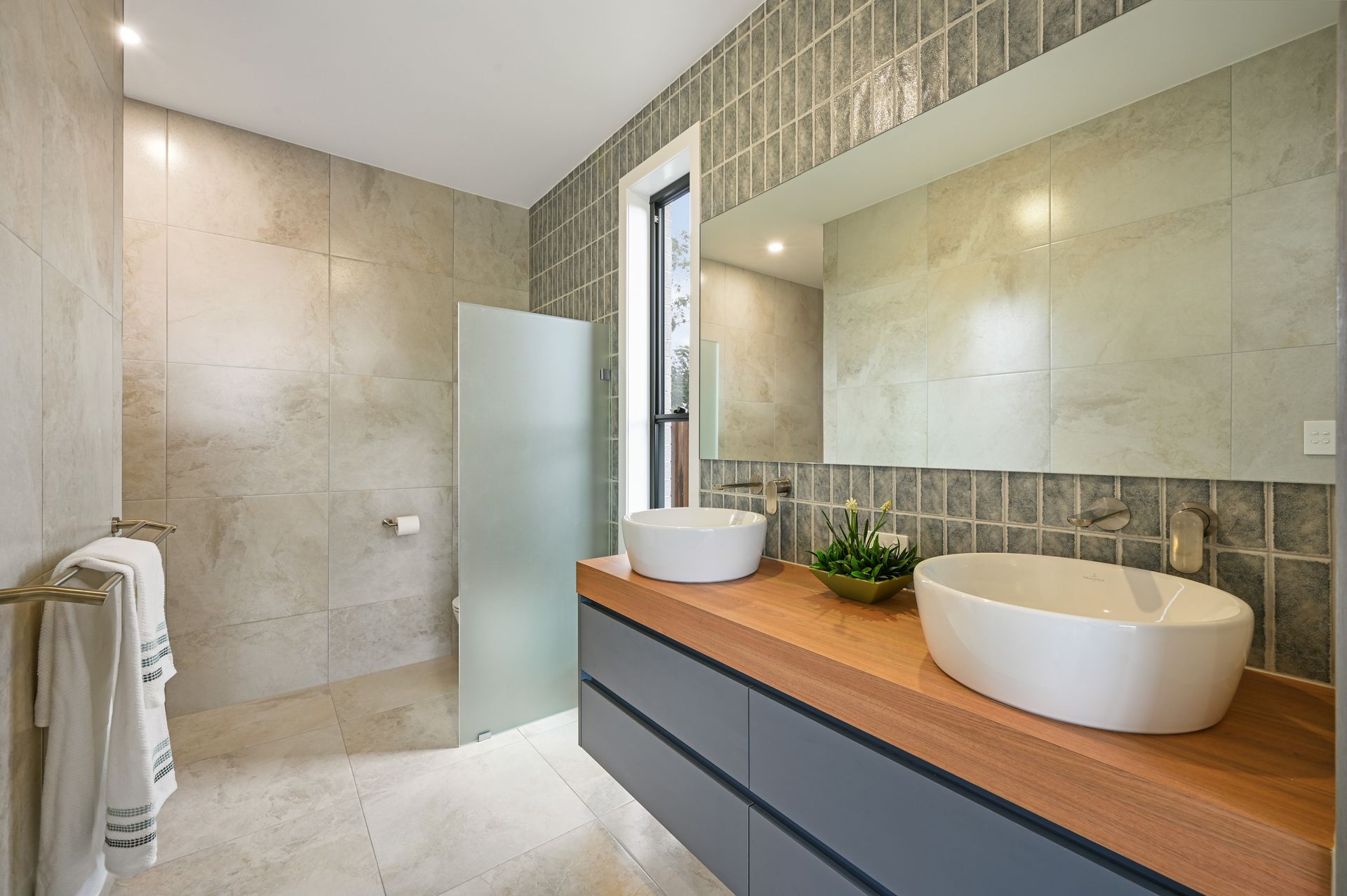 Modern bathroom with two white vessel sinks on a wooden vanity, grey walls, and frosted glass shower.