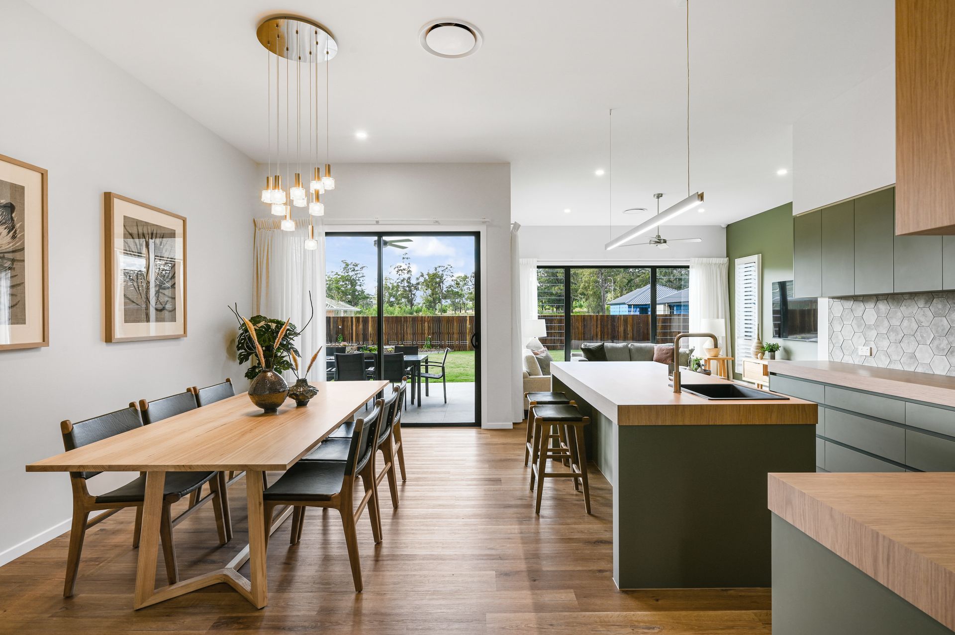 Dining room with wood table, chairs, and modern kitchen with dark green cabinets and a sliding glass door to the backyard.