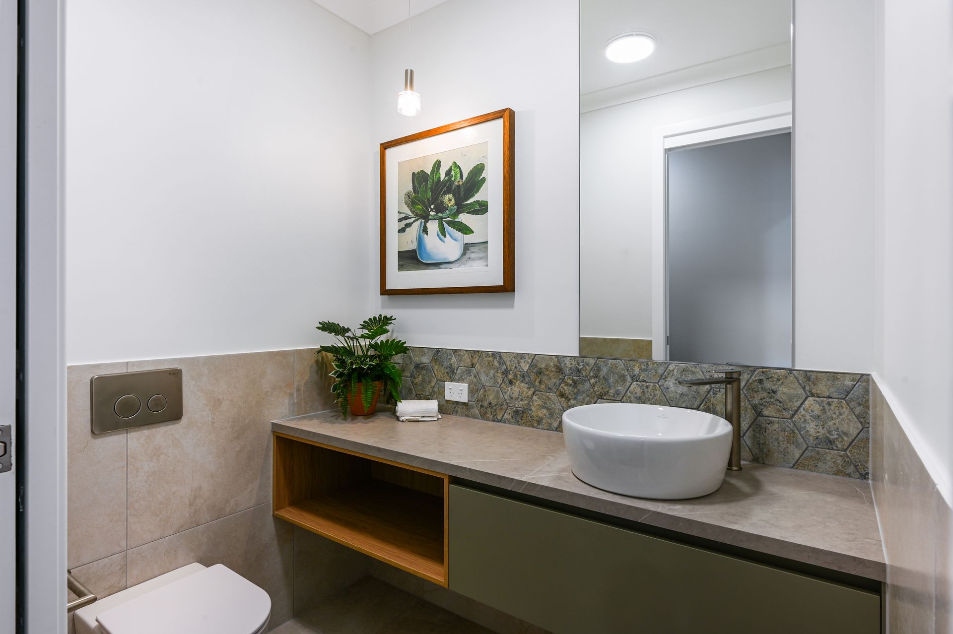 Bathroom with white walls, a grey vanity, and a round sink. Artwork and a small plant are on the counter.