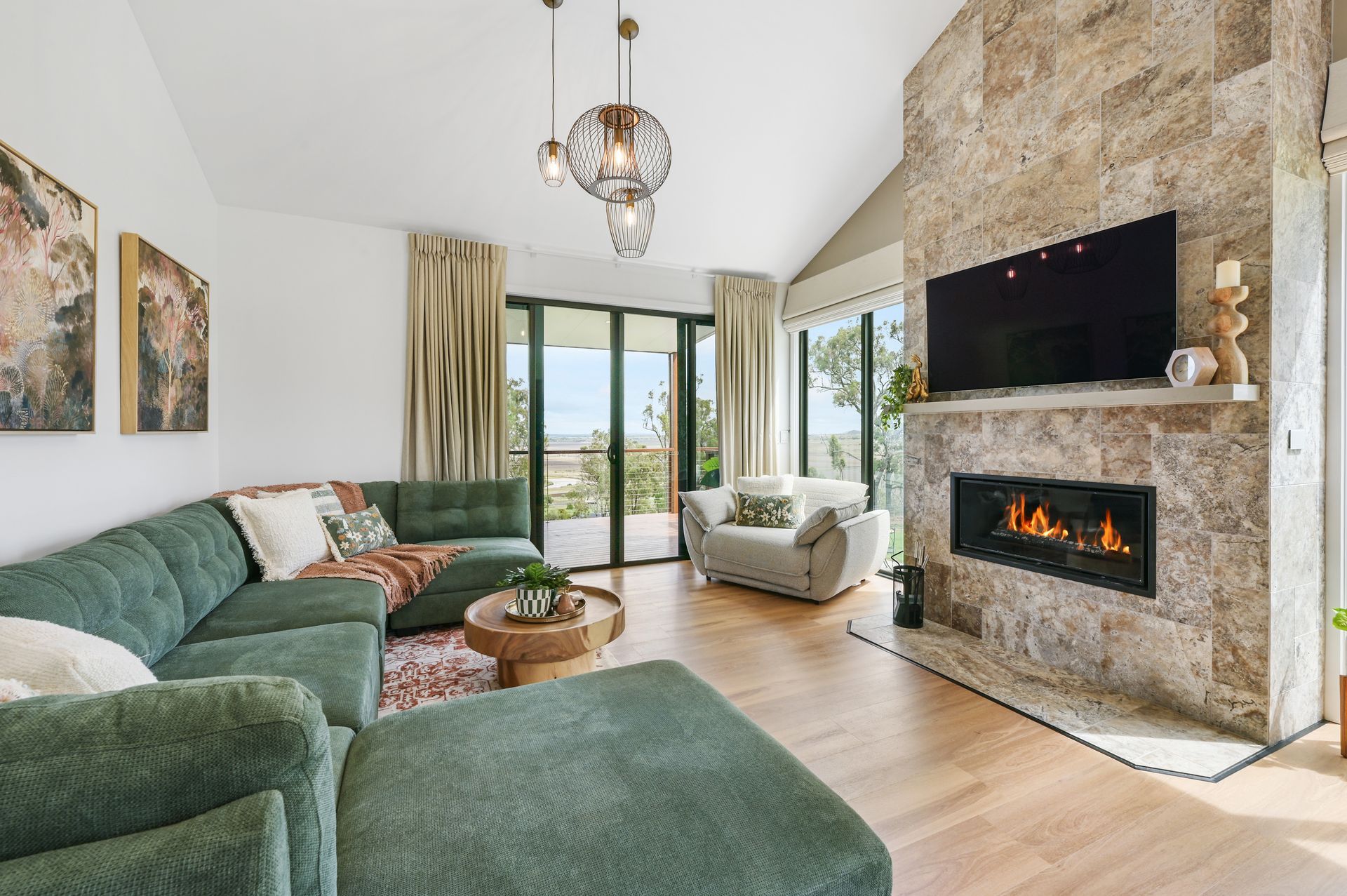 Living room with stone fireplace, green sectional, and view of trees.