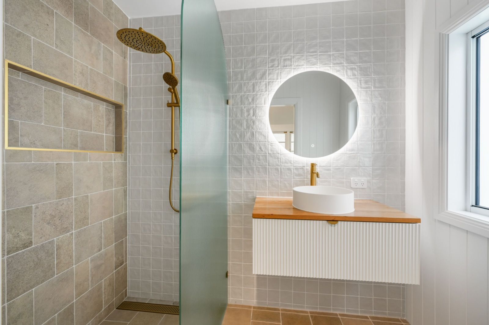 Modern bathroom with gold fixtures, round mirror, and white floating vanity.