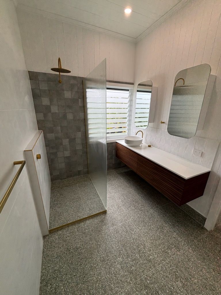 Bathroom with shower, vanity, and gold fixtures; gray and white tones.