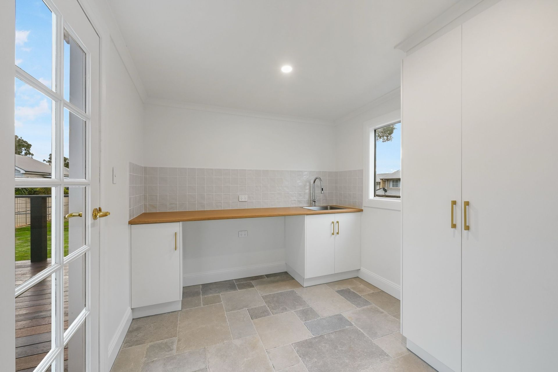 Laundry room with white cabinets, sink, wooden countertop, window, and door to a yard.