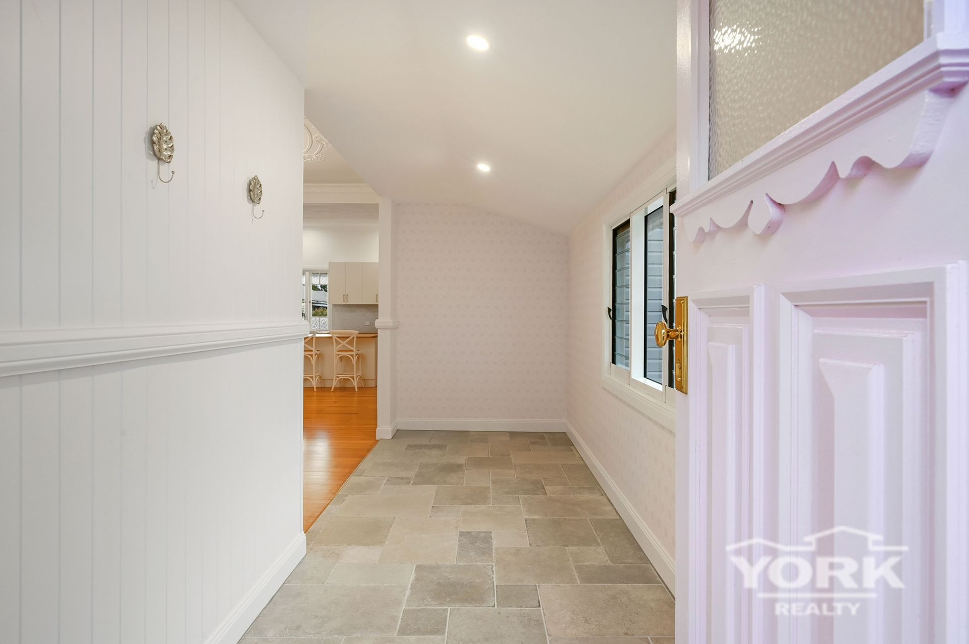 Entryway with stone tile floor, white walls and door frame, leading to a kitchen.