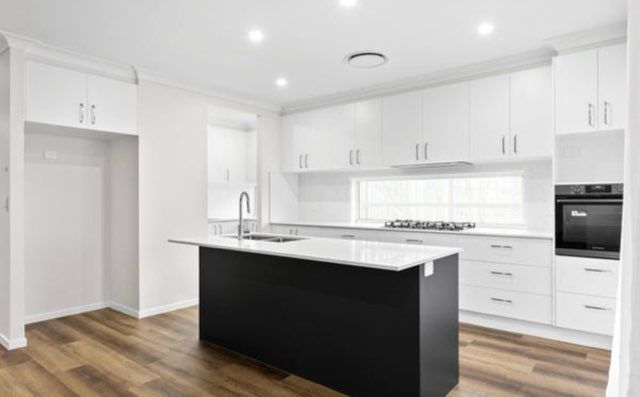Modern white kitchen with black island, hardwood floors, and built-in appliances.