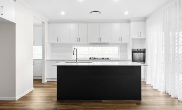 Modern white kitchen with black island, stainless steel faucet, and wooden floors.