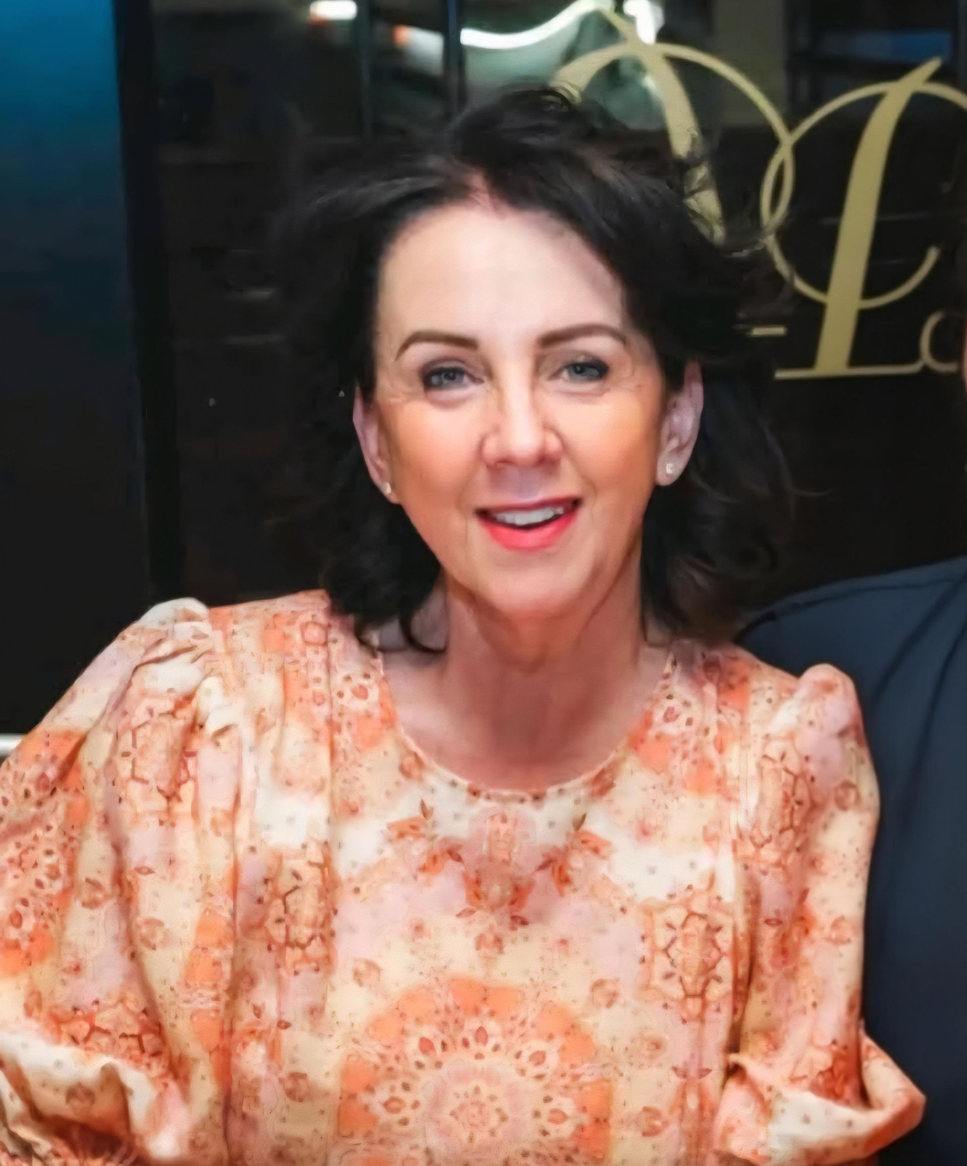 Woman with dark hair in a patterned peach top smiles.